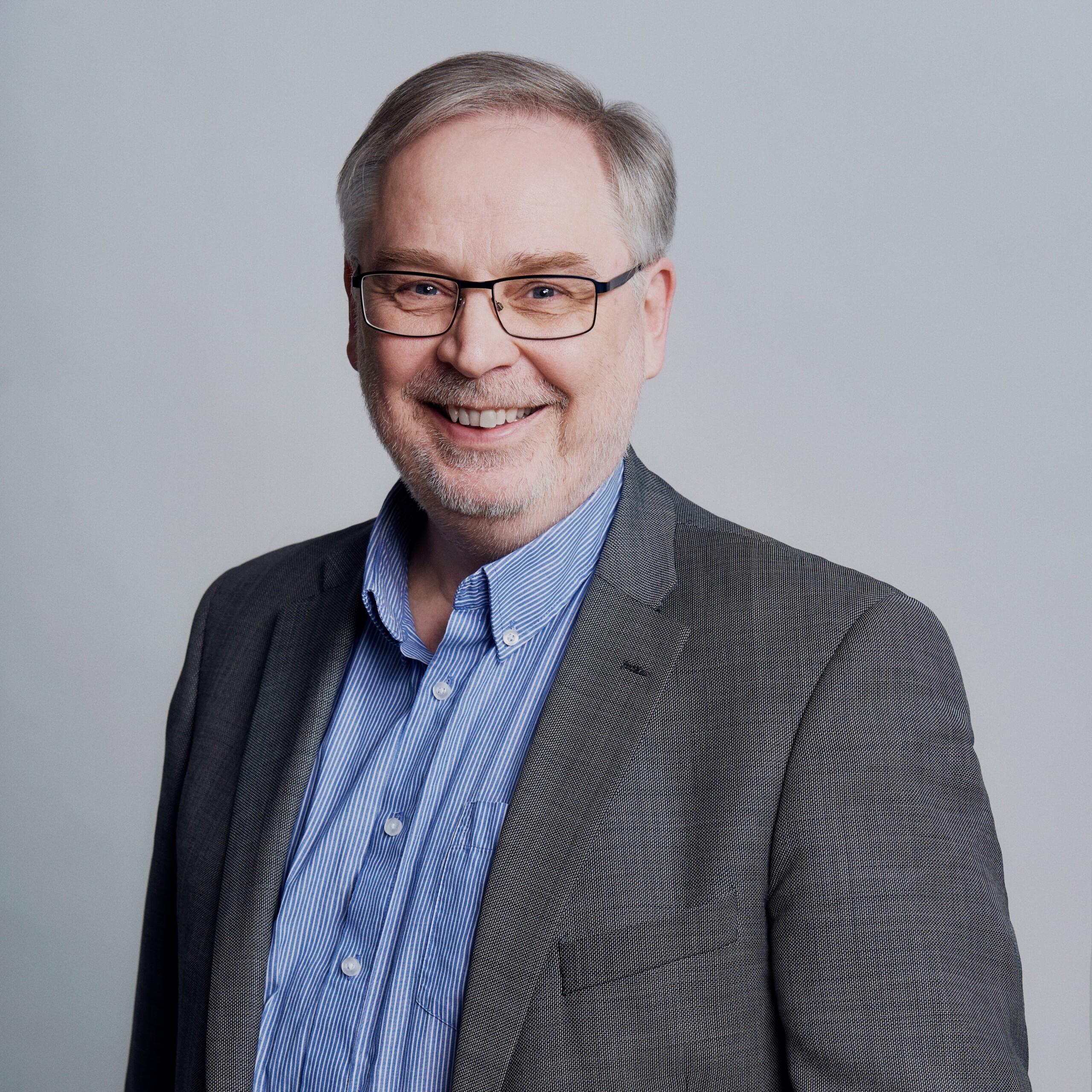Vanhempi henkilö harmaassa puvuntakissa ja sinisessä kauluspaidassa. Projektipäällikkö Mika Holmström.