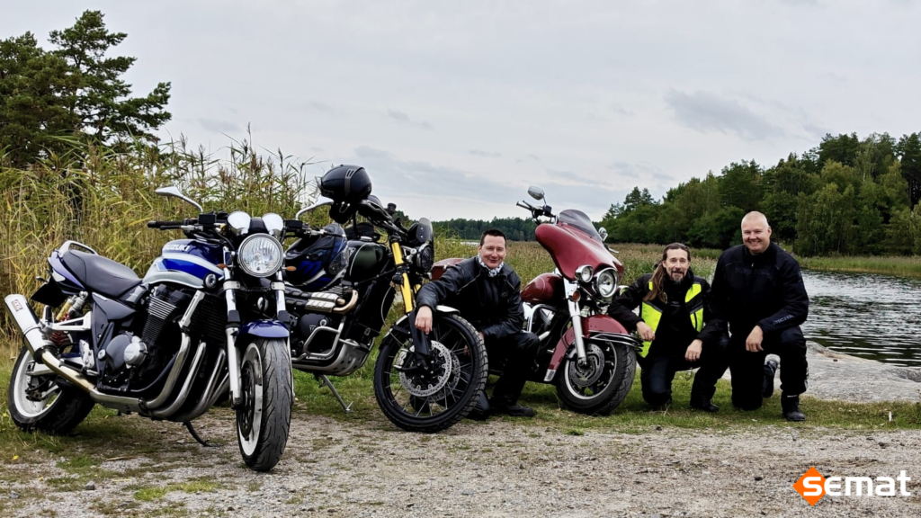 Moottoripyöriä, joiden vierellä kolme henkilöä kyykyssä. Taustalla järvimaisema.